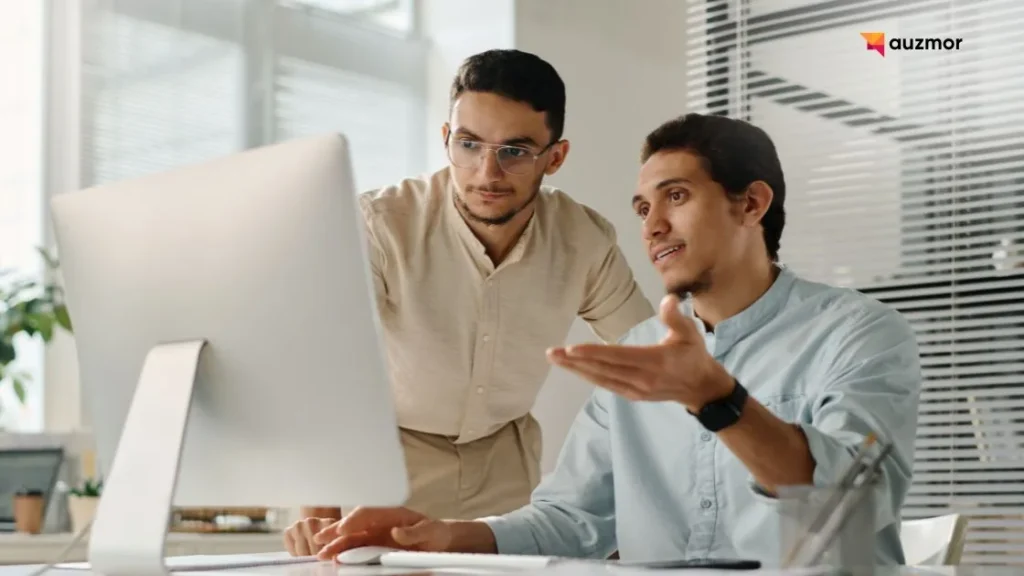 Two colleagues discussing work on a desktop computer in an office