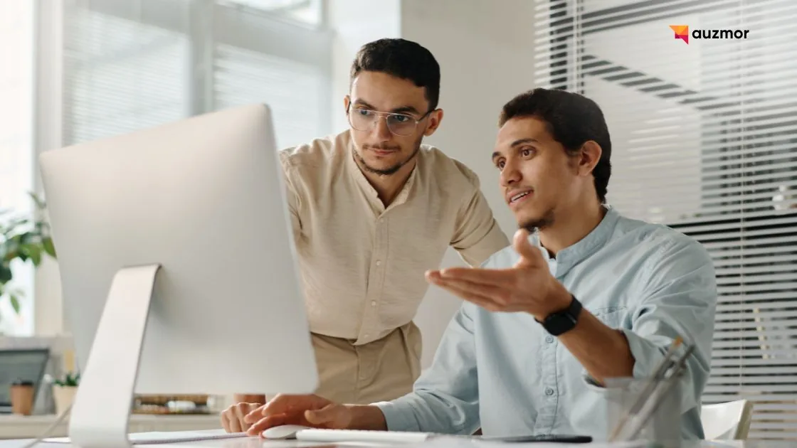 Two colleagues discussing work on a desktop computer in an office