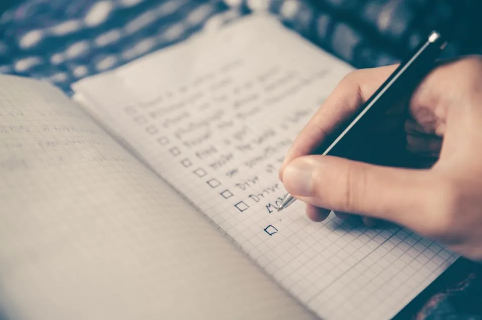 Hand writing a checklist of small daily goals in a notebook